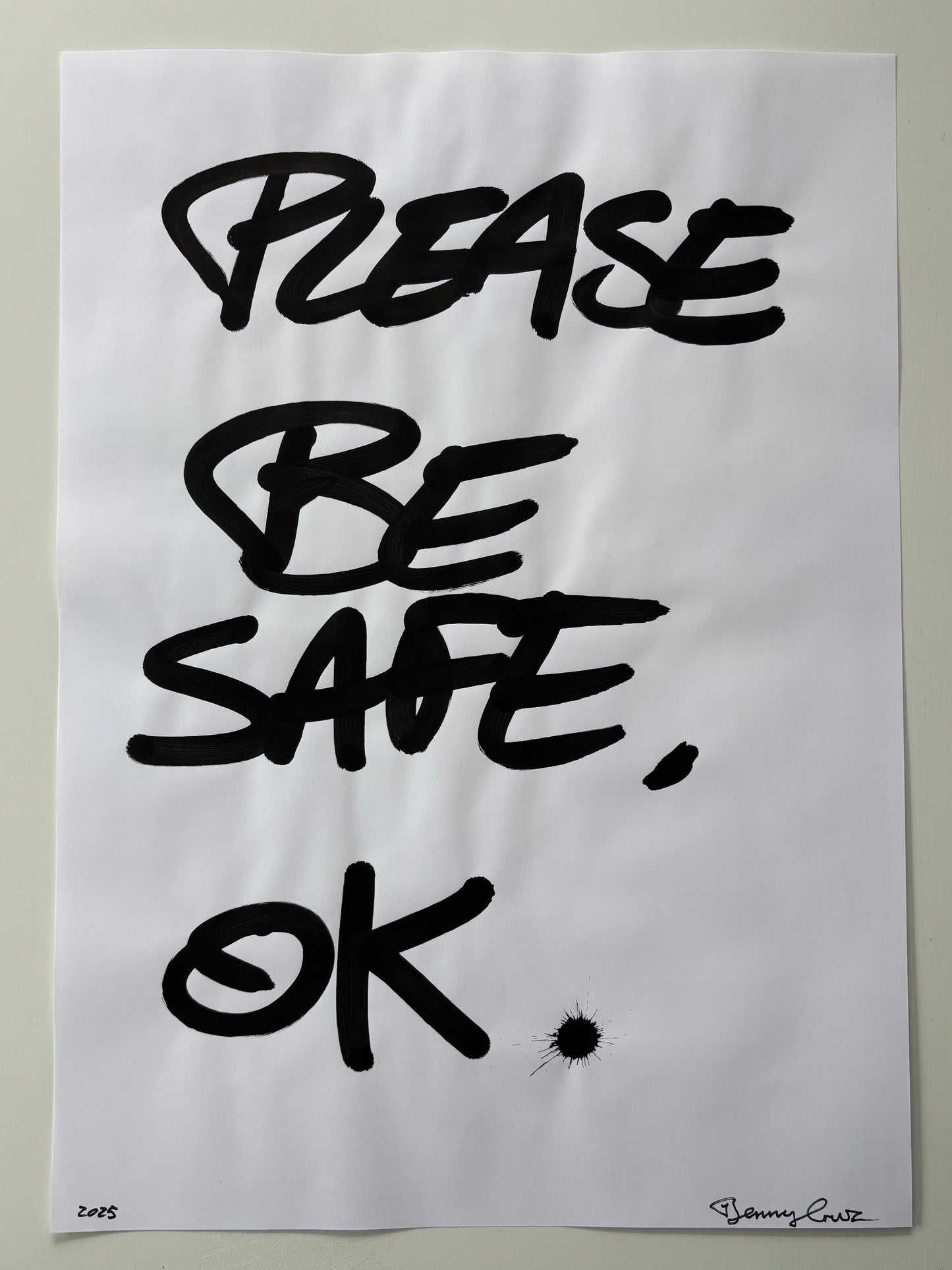 A white art print featuring the hand-lettered text 'PLEASE BE SAFE, OK' in bold black ink, displayed against a neutral light gray background.