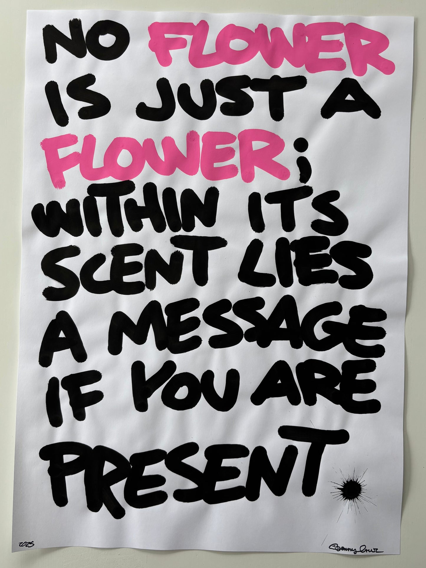 A white rectangular poster or print with hand-lettered black and pink text reading 'NO FLOWER IS JUST A FLOWER: WITHIN IT'S Scented A MESSAGE IF YOU ARE NOT PRESENT', photographed against a light neutral background.