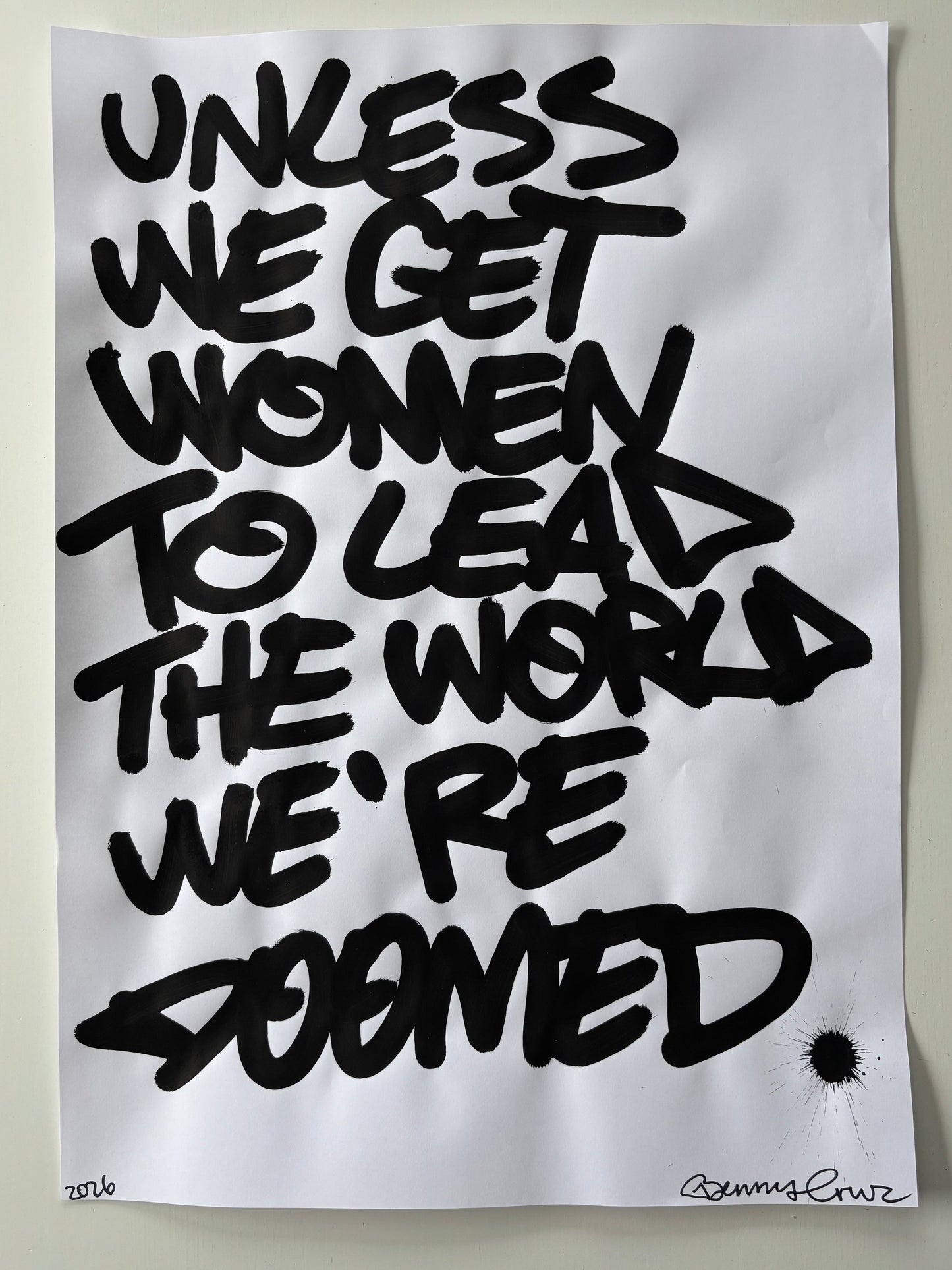 A square white art print or poster featuring bold black graffiti-style lettering that reads 'UNLESS WE GET WOMEN TO LEAD THE WORLD WE'RE DOMED,' photographed against a light neutral background.